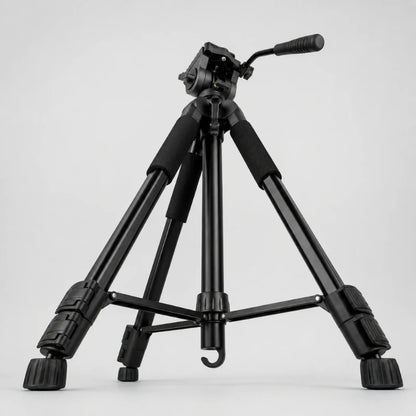 Trépied robuste noir en position basse sur fond gris, tête vidéo fluide noire avec levier, grips mousse, jambes très écartées vue trois quarts