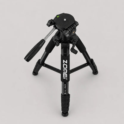Trépied Zomei noir en position très basse vu de dessus sur fond gris, tête panoramique avec niveau à bulle vert visible, jambes triangulaires très écartées