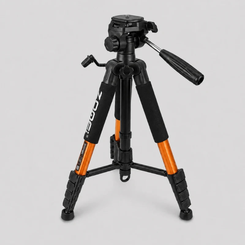 Trépied Zomei orange et noir en position très basse sur fond gris, tête panoramique 3 voies noire avec levier, grips mousse noirs, jambes oranges écartées, vue trois quarts
