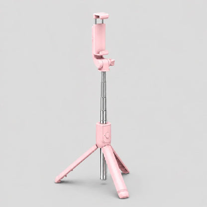 Mini trépied téléphone rose entièrement déplié posé sur fond gris, vue de face montrant la tige télescopique argentée et les trois pieds roses écartés