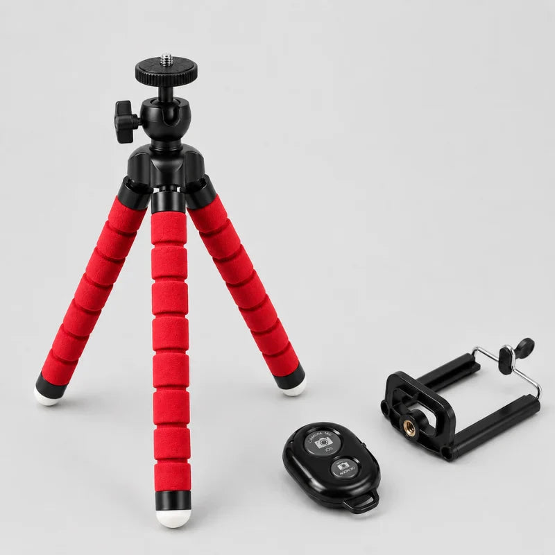 Mini trépied flexible rouge avec rotule à bille noire, support téléphone noir et télécommande Bluetooth noire posée a côté, sur fond gris