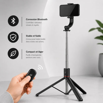 Trépied noir pour téléphone avec smartphone fixé et télécommande Bluetooth dans une main, fond intérieur lumineux