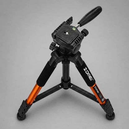 Trépied orange et noir en position basse déployé avec rotule panoramique, niveau à bulle, fond gris