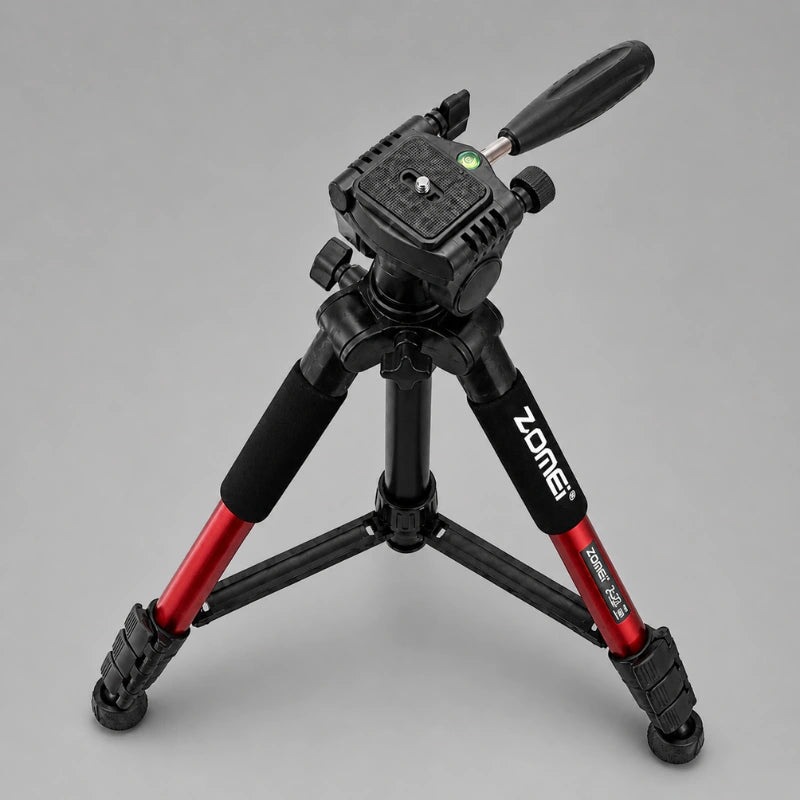 Trépied Zomei rouge en position basse sur fond gris, tête 3 voies noire avec levier, grips mousse, vue trois quarts