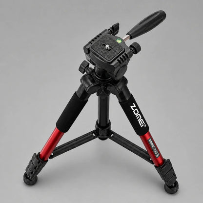 Trépied Zomei rouge en position basse sur fond gris, tête 3 voies noire avec levier, grips mousse, vue trois quarts